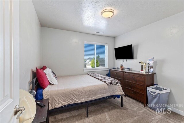 carpeted bedroom featuring a textured ceiling, visible vents, and baseboards