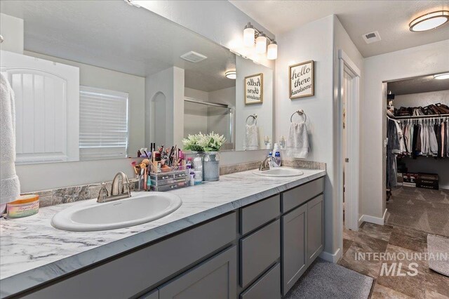 bathroom with a sink, a shower stall, double vanity, and visible vents