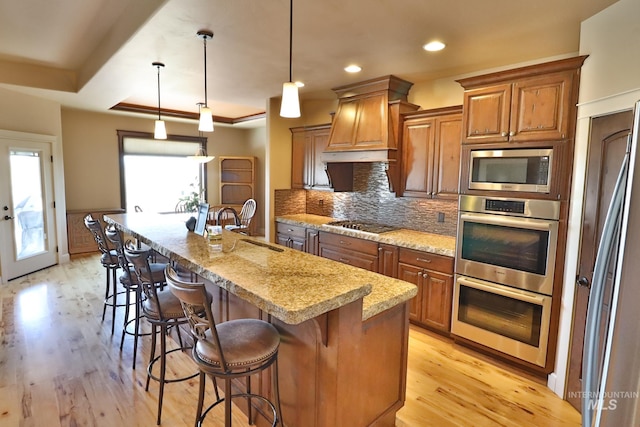 924 Main St S, Kimberly, ID 83341 - kitchen featuring appliances with stainless steel finishes, premium range hood, brown cabinetry, light wood-style flooring, and recessed lighting