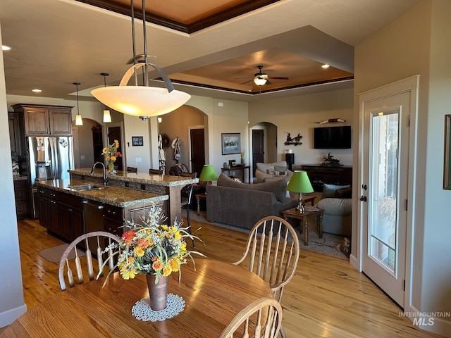 dining room featuring light hardwood / wood-style flooring, sink, ceiling fan, and a tray ceiling