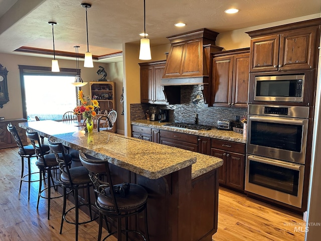 kitchen with light stone countertops, light hardwood / wood-style floors, a center island with sink, and hanging light fixtures