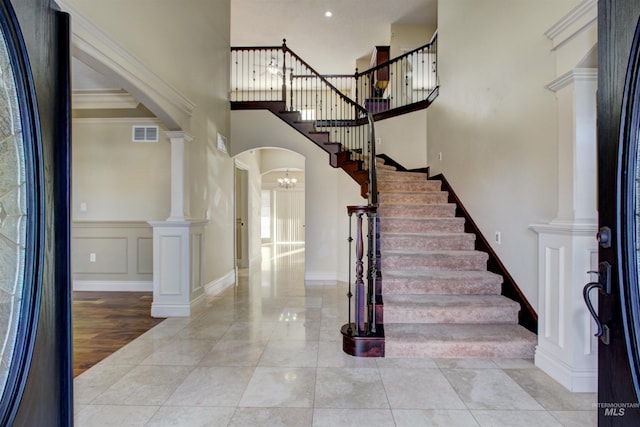 tiled entryway with ornamental molding, a notable chandelier, a high ceiling, and ornate columns