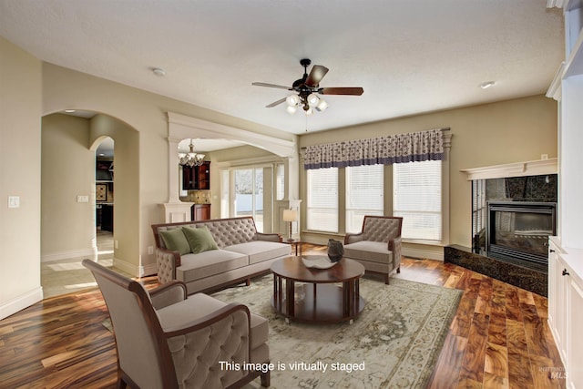 living room with dark wood-type flooring, a high end fireplace, and ceiling fan with notable chandelier