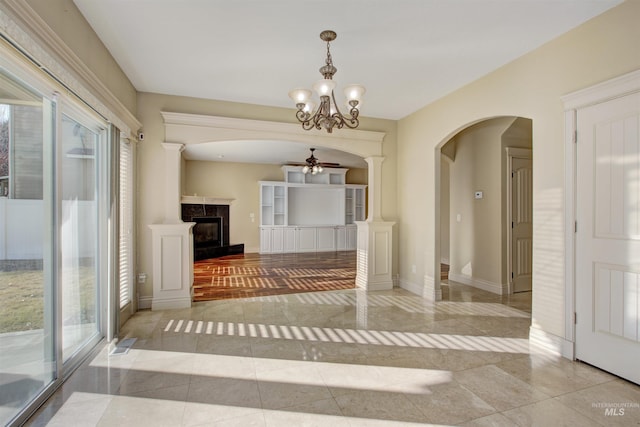 unfurnished dining area with ceiling fan with notable chandelier, light tile patterned floors, a wealth of natural light, and ornate columns