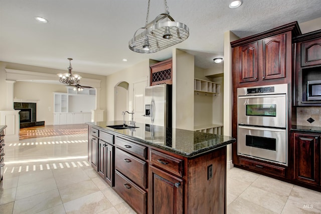 kitchen with stainless steel appliances, sink, an island with sink, a premium fireplace, and hanging light fixtures