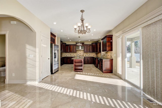 kitchen featuring a chandelier, pendant lighting, wall chimney range hood, tasteful backsplash, and stainless steel refrigerator with ice dispenser