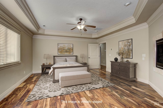 bedroom featuring a textured ceiling, a raised ceiling, crown molding, dark hardwood / wood-style flooring, and ceiling fan