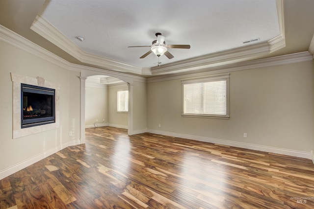 spare room with a raised ceiling, crown molding, dark hardwood / wood-style flooring, a fireplace, and ceiling fan