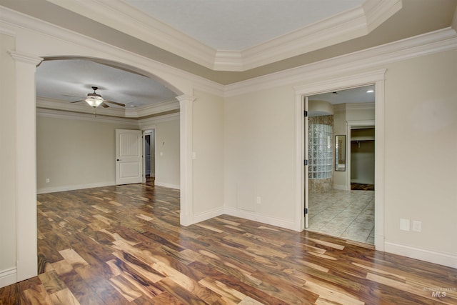 empty room with ornate columns, ceiling fan, hardwood / wood-style flooring, ornamental molding, and a tray ceiling