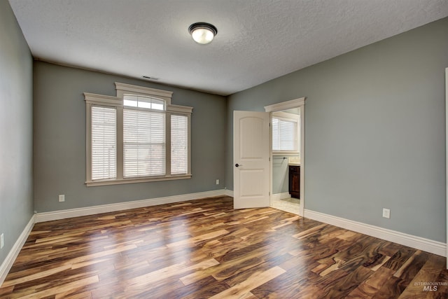 empty room with a textured ceiling, plenty of natural light, and dark wood-type flooring