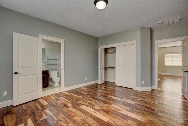 unfurnished bedroom with hardwood / wood-style floors, a closet, and ensuite bath