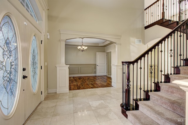 tiled foyer entrance with decorative columns, a notable chandelier, and ornamental molding