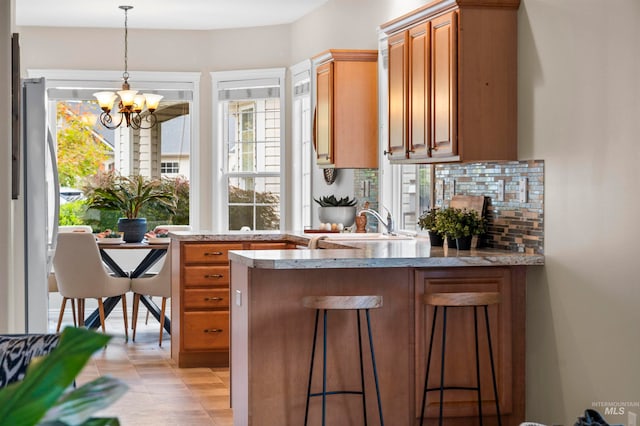 kitchen featuring kitchen peninsula, hanging light fixtures, a kitchen breakfast bar, an inviting chandelier, and stainless steel refrigerator