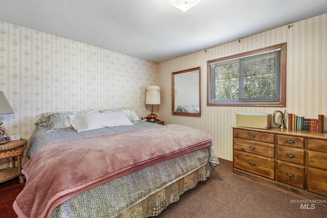 bedroom featuring wallpapered walls, dark carpet, and a textured ceiling