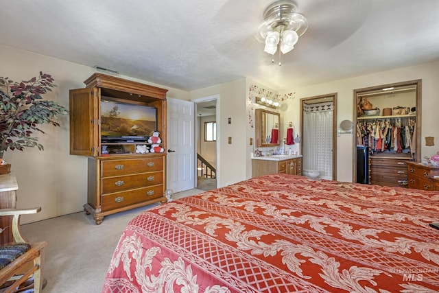 bedroom with ensuite bath, ceiling fan, a textured ceiling, and light colored carpet