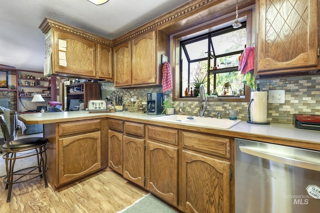 kitchen featuring a peninsula, a sink, light countertops, dishwasher, and brown cabinetry