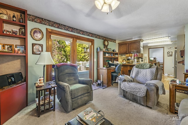 living area with light carpet, a ceiling fan, and a textured ceiling