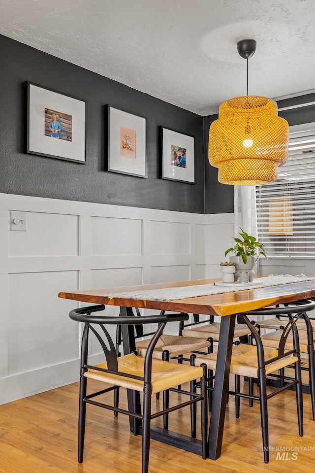 dining room with a decorative wall, wainscoting, a textured ceiling, and light wood-type flooring