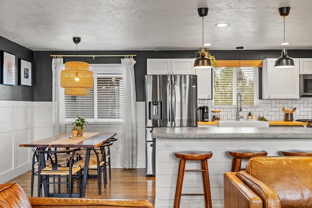 kitchen featuring a kitchen bar, wainscoting, wood finished floors, stainless steel appliances, and a sink