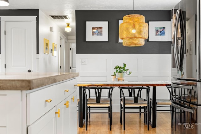 dining space with visible vents, light wood-style floors, a wainscoted wall, and a decorative wall