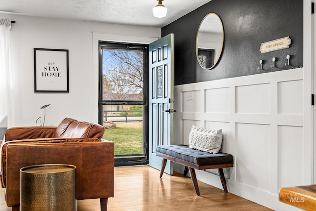 entryway featuring light wood finished floors, a decorative wall, wainscoting, and a textured ceiling