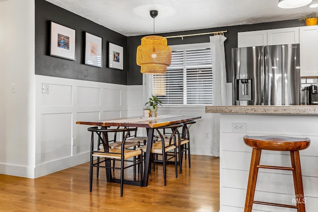 dining area featuring a decorative wall, light wood-style floors, and wainscoting