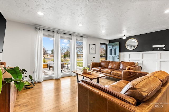 living room with a wainscoted wall, a textured ceiling, and light wood-style flooring