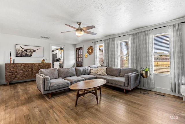 living room with visible vents, a textured ceiling, a ceiling fan, and wood-type flooring