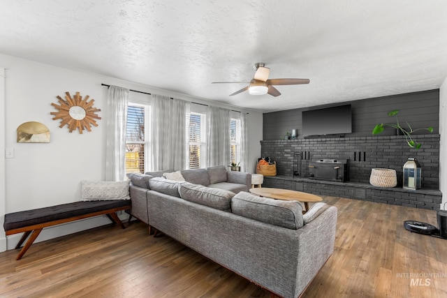 living room with a textured ceiling, a wood stove, a ceiling fan, and hardwood / wood-style floors