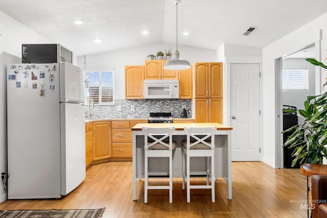 kitchen featuring white appliances, light brown cabinets, light countertops, vaulted ceiling, and light wood-style floors