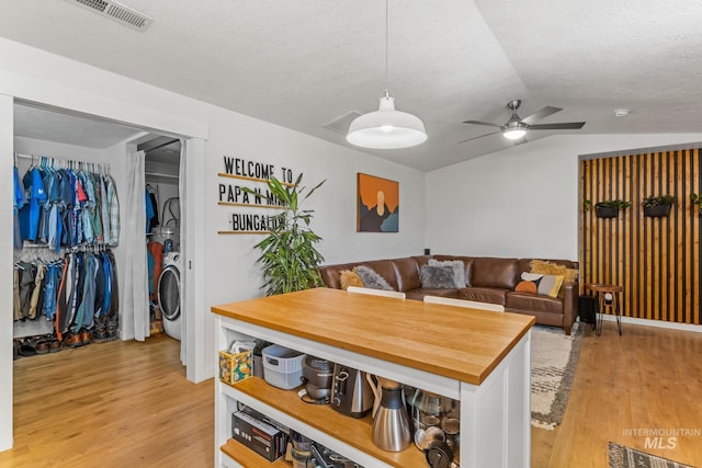 kitchen featuring visible vents, butcher block countertops, light wood finished floors, lofted ceiling, and washer / dryer