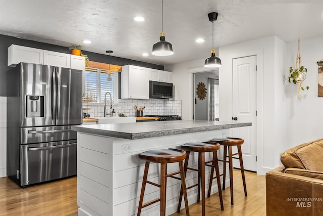 kitchen featuring a sink, light wood-style floors, appliances with stainless steel finishes, a kitchen breakfast bar, and tasteful backsplash