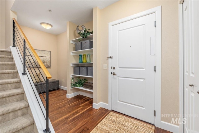 foyer entrance featuring dark wood-style floors, baseboards, and stairway