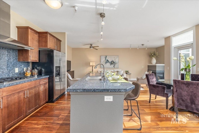 kitchen featuring a breakfast bar area, stainless steel appliances, a sink, backsplash, and wall chimney exhaust hood