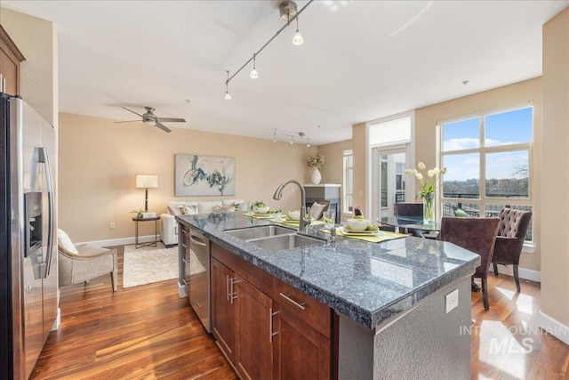 kitchen featuring dark wood-style flooring, appliances with stainless steel finishes, open floor plan, a kitchen island with sink, and a sink