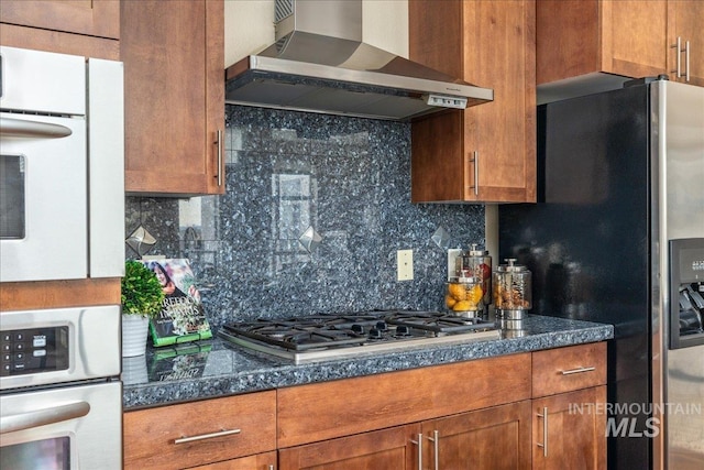 kitchen featuring wall chimney range hood, tasteful backsplash, appliances with stainless steel finishes, and brown cabinets