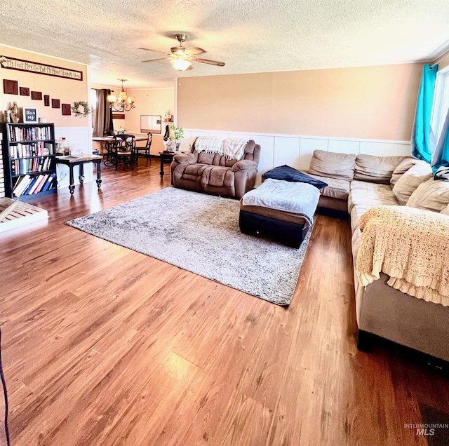 living room with ceiling fan with notable chandelier, wood finished floors, and a textured ceiling