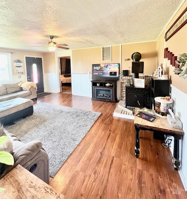 living room featuring visible vents, a wainscoted wall, a ceiling fan, wood finished floors, and a wood stove