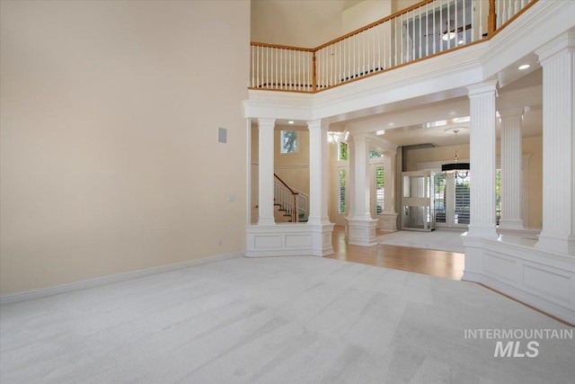 carpeted entryway featuring ornate columns, a high ceiling, and stairs