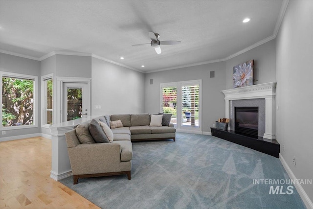 living area featuring ceiling fan, baseboards, recessed lighting, a glass covered fireplace, and ornamental molding