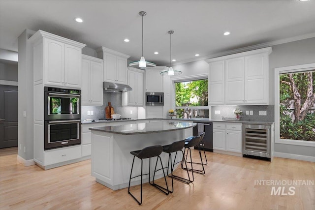 kitchen featuring beverage cooler, multiple ovens, stainless steel microwave, dishwasher, and under cabinet range hood