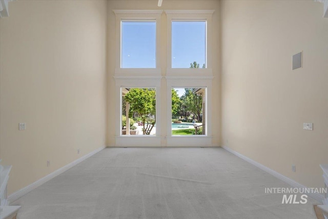spare room featuring carpet flooring, a high ceiling, and baseboards