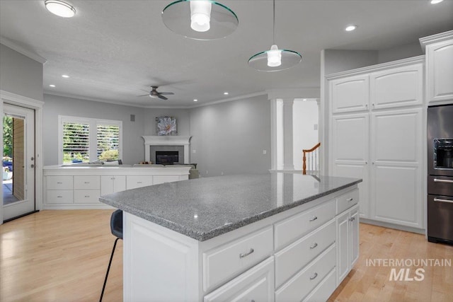 kitchen featuring black fridge, a kitchen island, a ceiling fan, light wood-style flooring, and ornamental molding