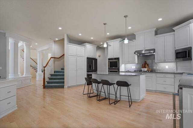 kitchen featuring under cabinet range hood, white cabinets, a kitchen breakfast bar, decorative backsplash, and a center island