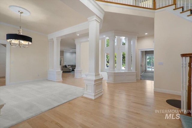 entryway with decorative columns, light wood-style flooring, a high ceiling, ornamental molding, and baseboards