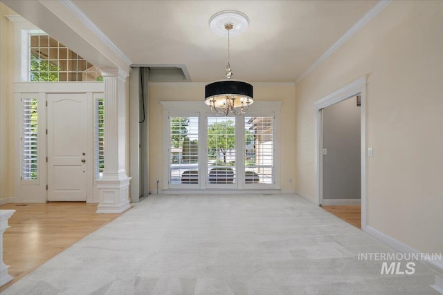 carpeted entrance foyer with a chandelier, ornamental molding, decorative columns, and baseboards