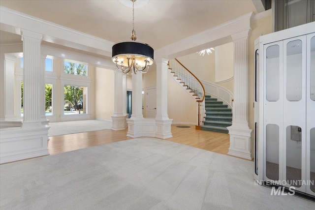 foyer featuring decorative columns, stairs, wood finished floors, a chandelier, and ornamental molding