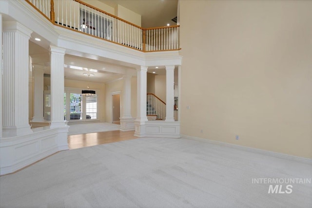 unfurnished living room featuring ornate columns, carpet flooring, and a high ceiling
