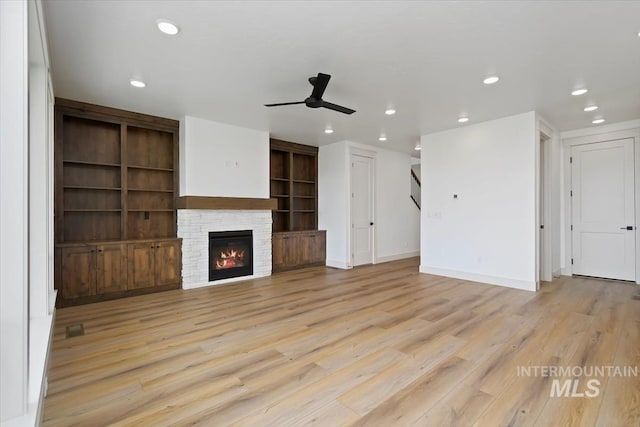 unfurnished living room featuring ceiling fan, built in shelves, a fireplace, and light hardwood / wood-style flooring