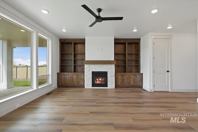 unfurnished living room featuring a stone fireplace, ceiling fan, and light hardwood / wood-style flooring